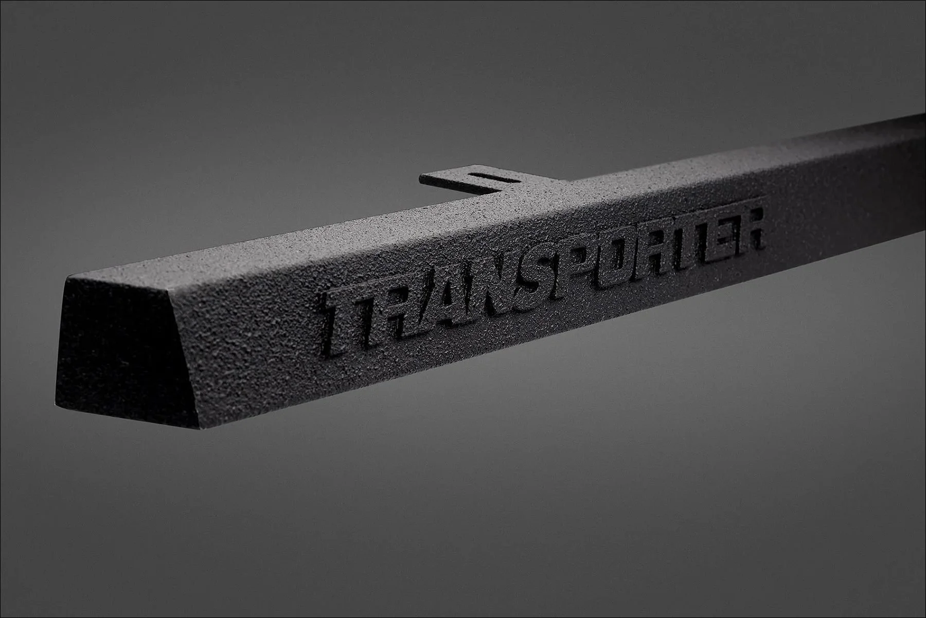 Dark grey rectangular object with embossed text reading "TRANSPORTER" viewed on a gradient background.