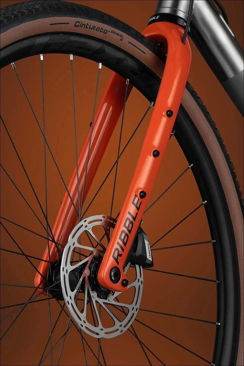 Close-up of an orange bicycle fork and front wheel with disc brake against an orange background.