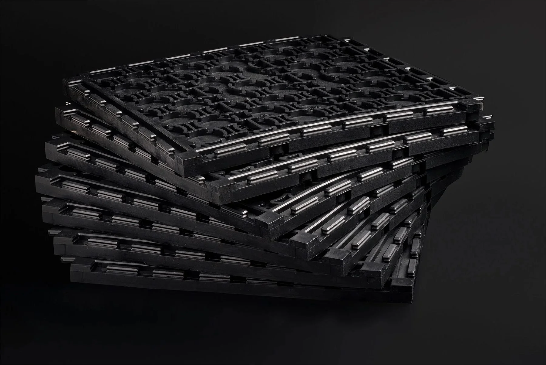 Stacked black rectangular mechanical components arranged in a cascading stack against a dark background