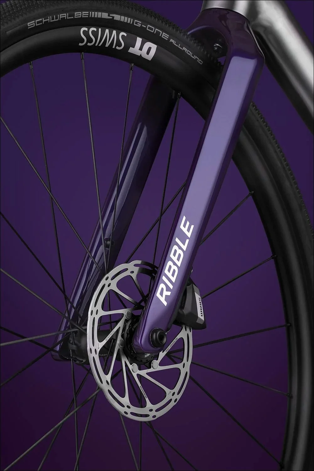 Close-up of a purple bicycle fork and front wheel with disc brake against a purple background.
