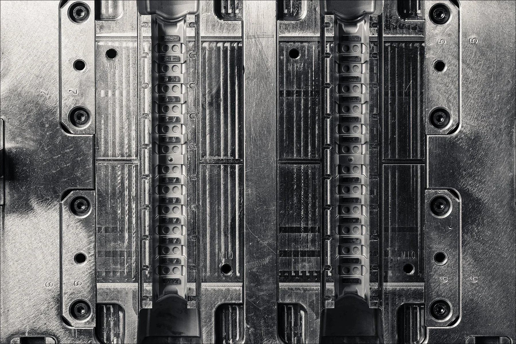 Black and white close-up of an industrial die or mould with symmetrical grooves and cavities.