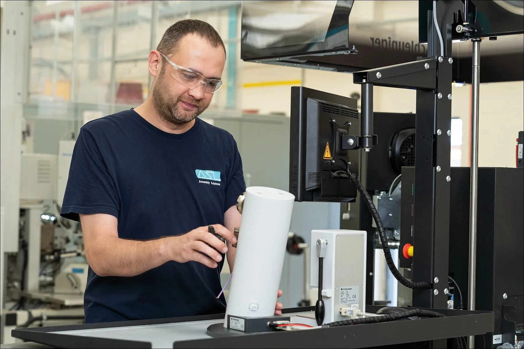 Engineer operating an industrial testing machine with a cylindrical component in a factory.