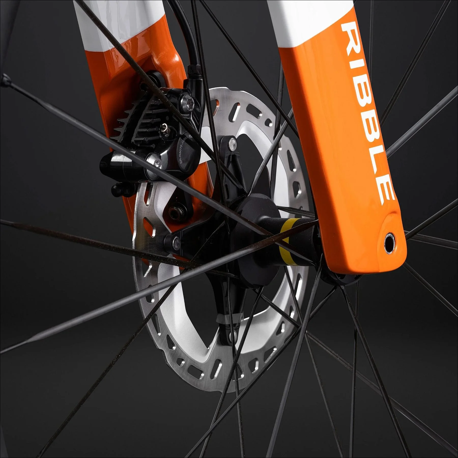 Close-up of a bright orange bicycle fork and disc brake rotor against a dark background.