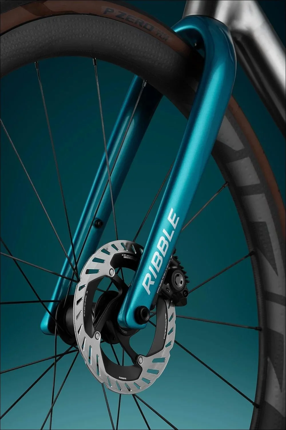 Close-up of a teal bicycle fork and front wheel with disc brake against a dark background.