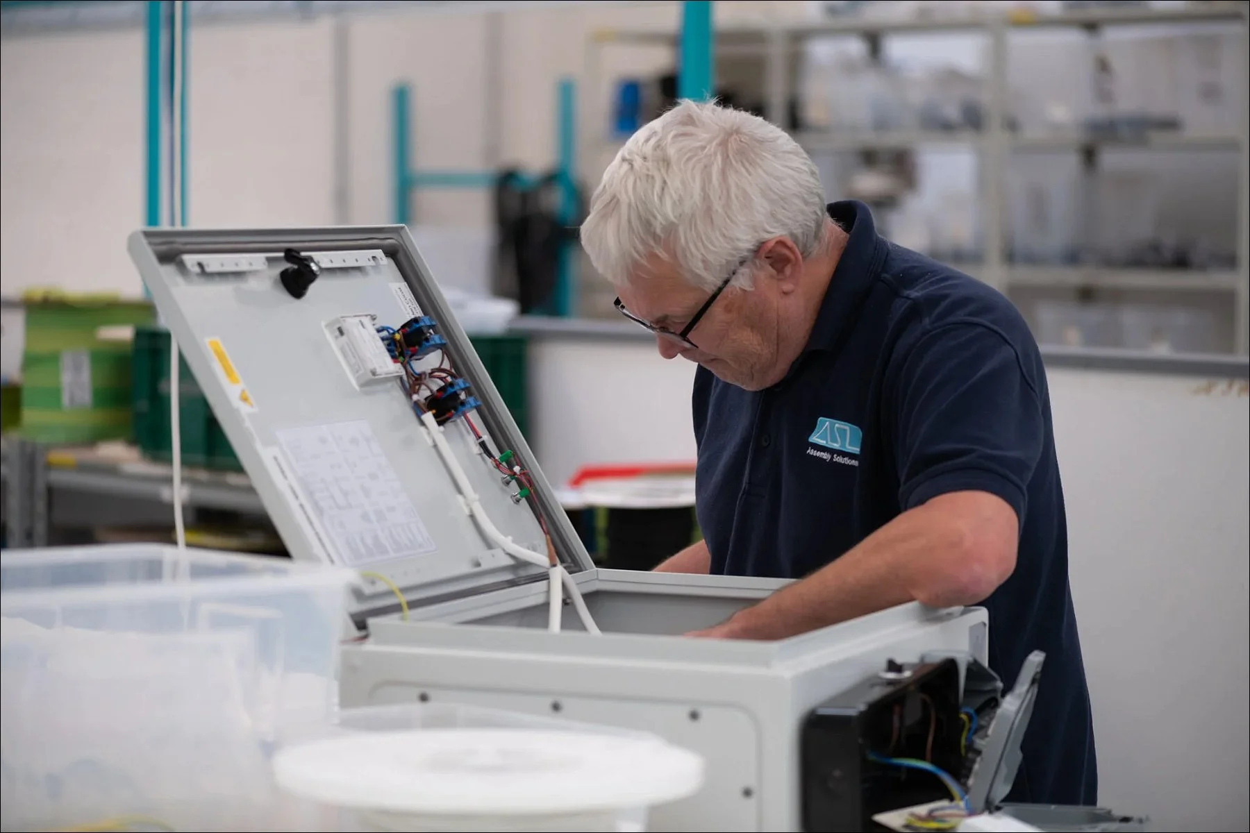 Technician assembling or inspecting electronic equipment at a factory workstation.