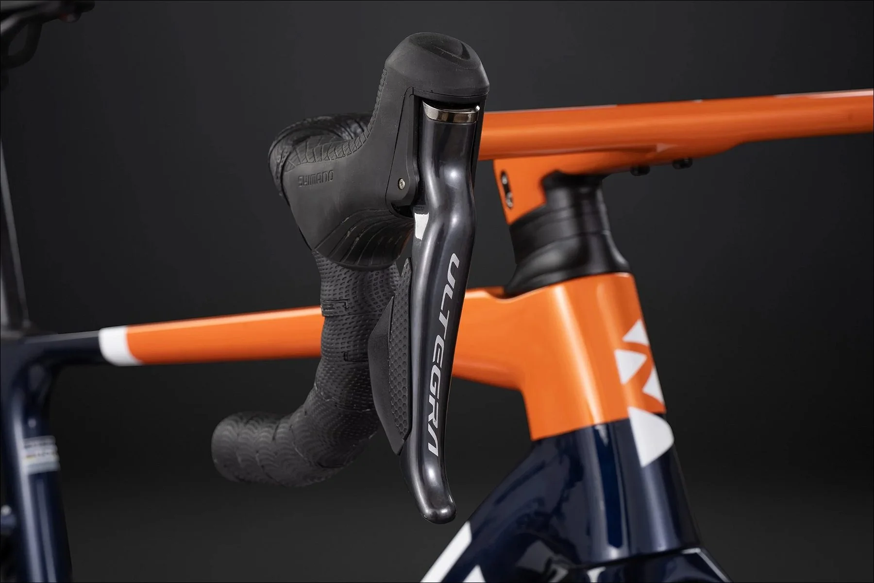 Close-up of a bicycle handlebars and orange top tube with brake lever against a dark background.