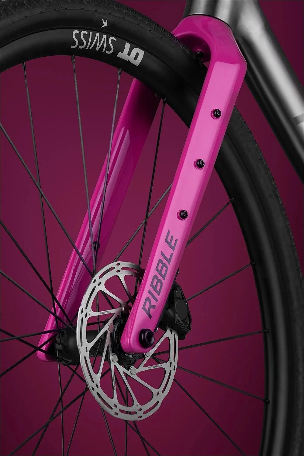 Close-up of a pink bicycle fork and front wheel with disc brake against a dark background.