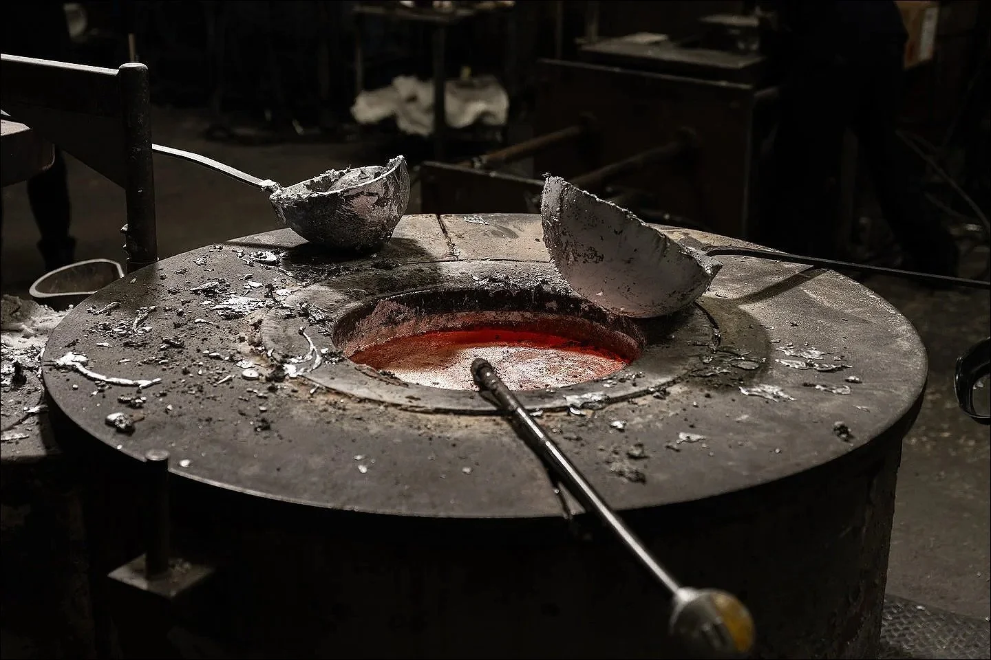 Molten metal glowing in a circular mold with metal ladles resting on top, inside an industrial foundry.