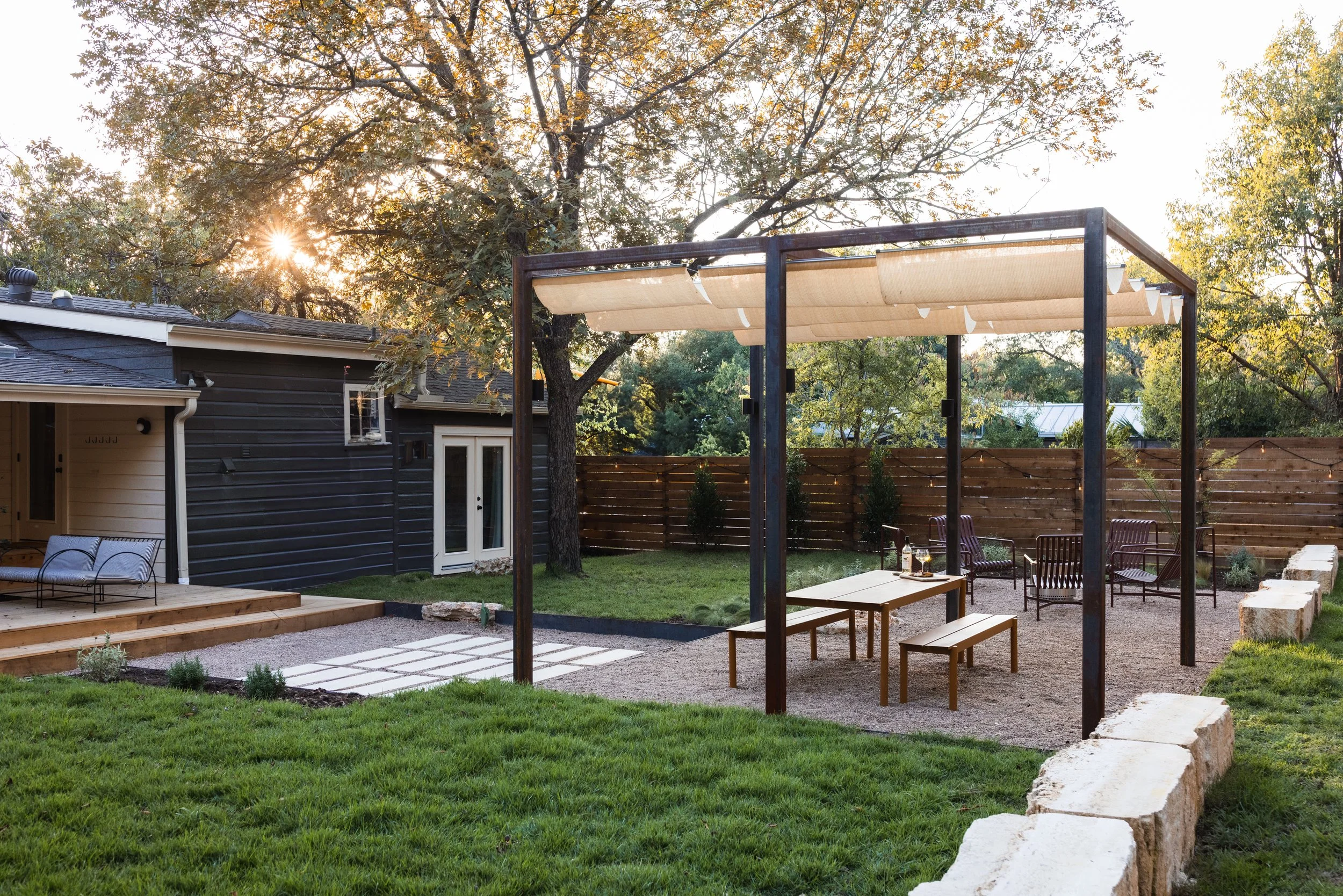 Backyard cedar deck with cedar fence, trees, grass, an outdoor seating area, and a shaded pergola with outdoor furniture during sunset.
