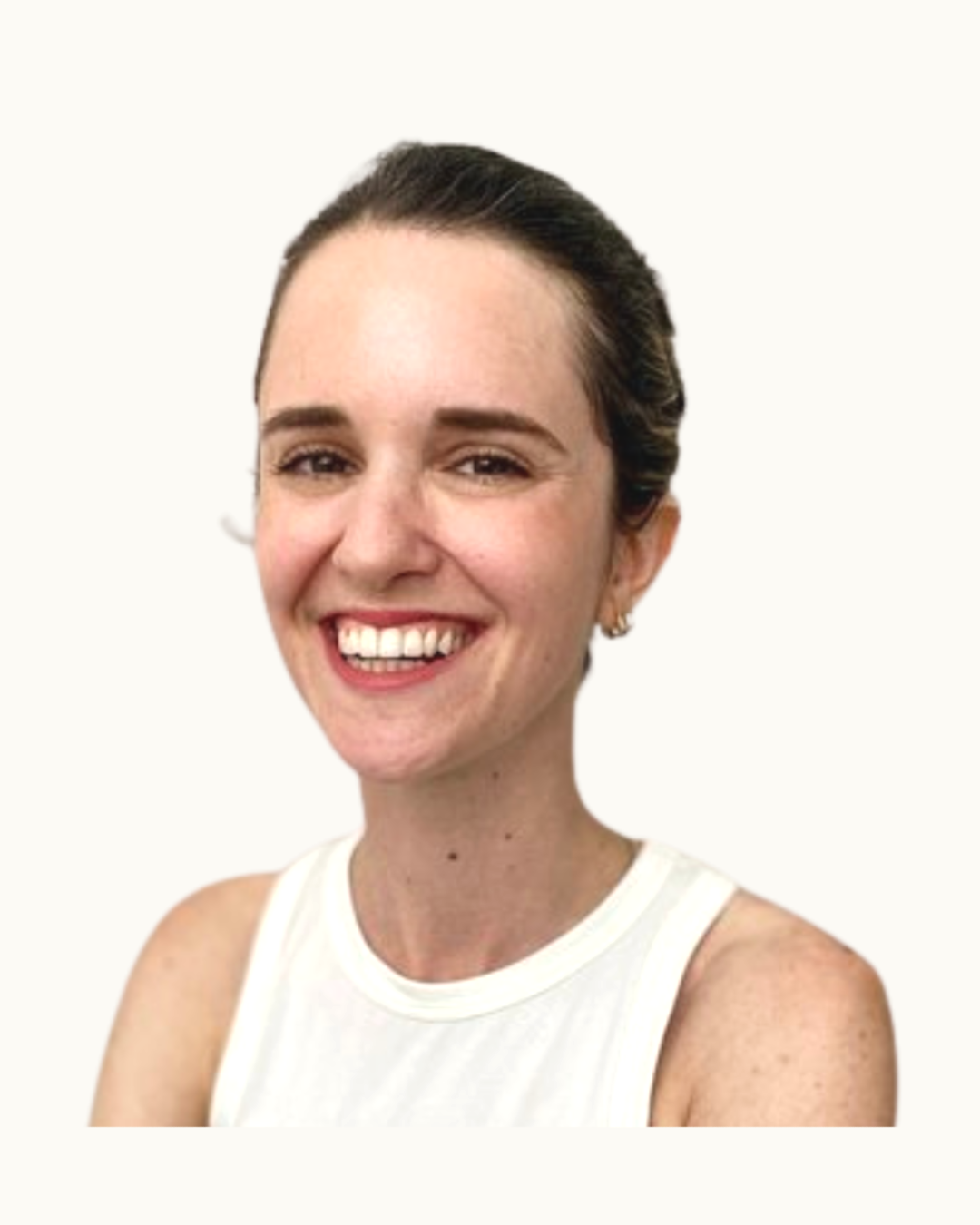 A smiling woman with brown hair tied back, wearing a sleeveless white top and earrings, standing with arms crossed against a plain light-colored wall.