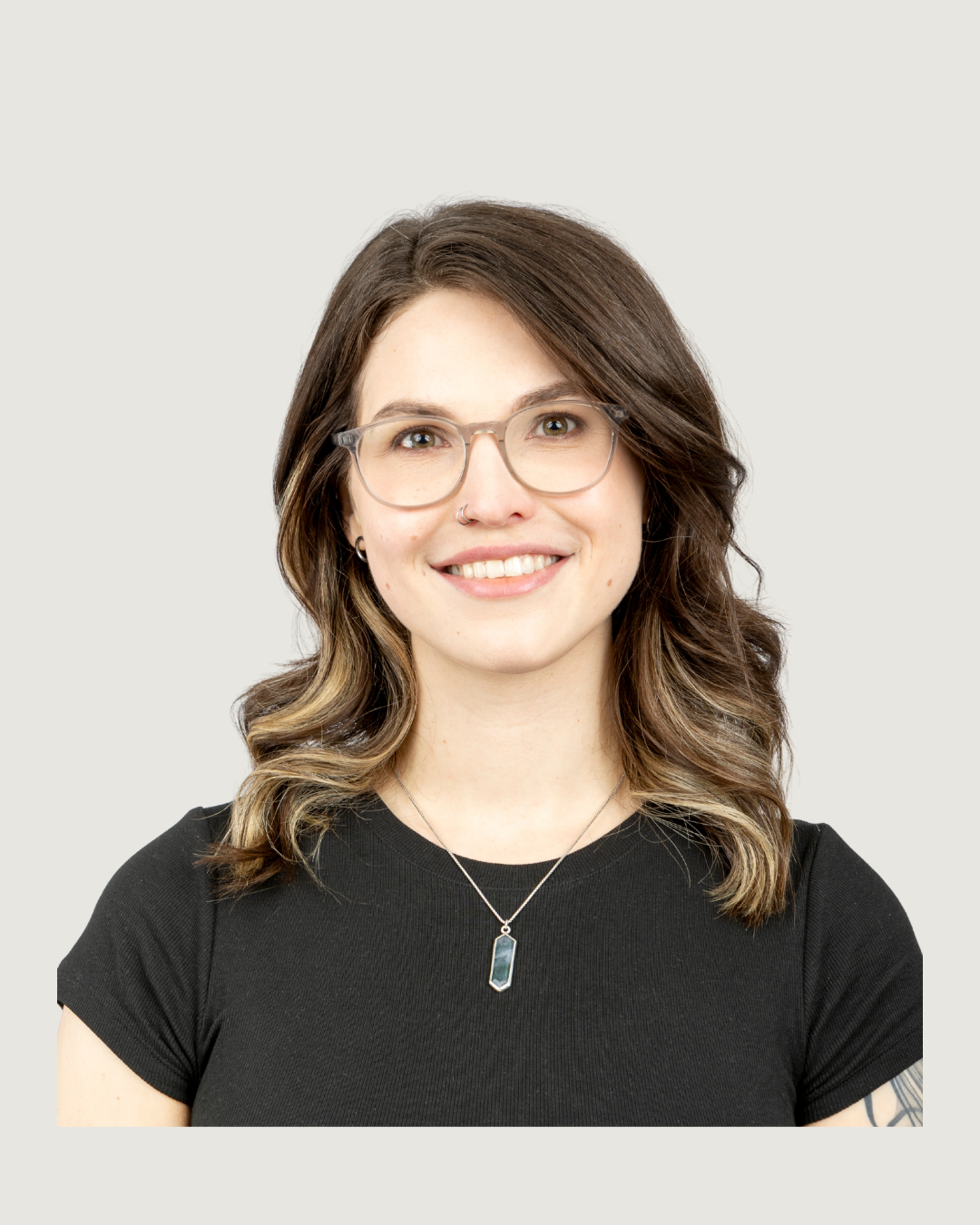 A woman with brown hair, glasses, and a nose ring wearing a black shirt and necklace smiling at the camera.