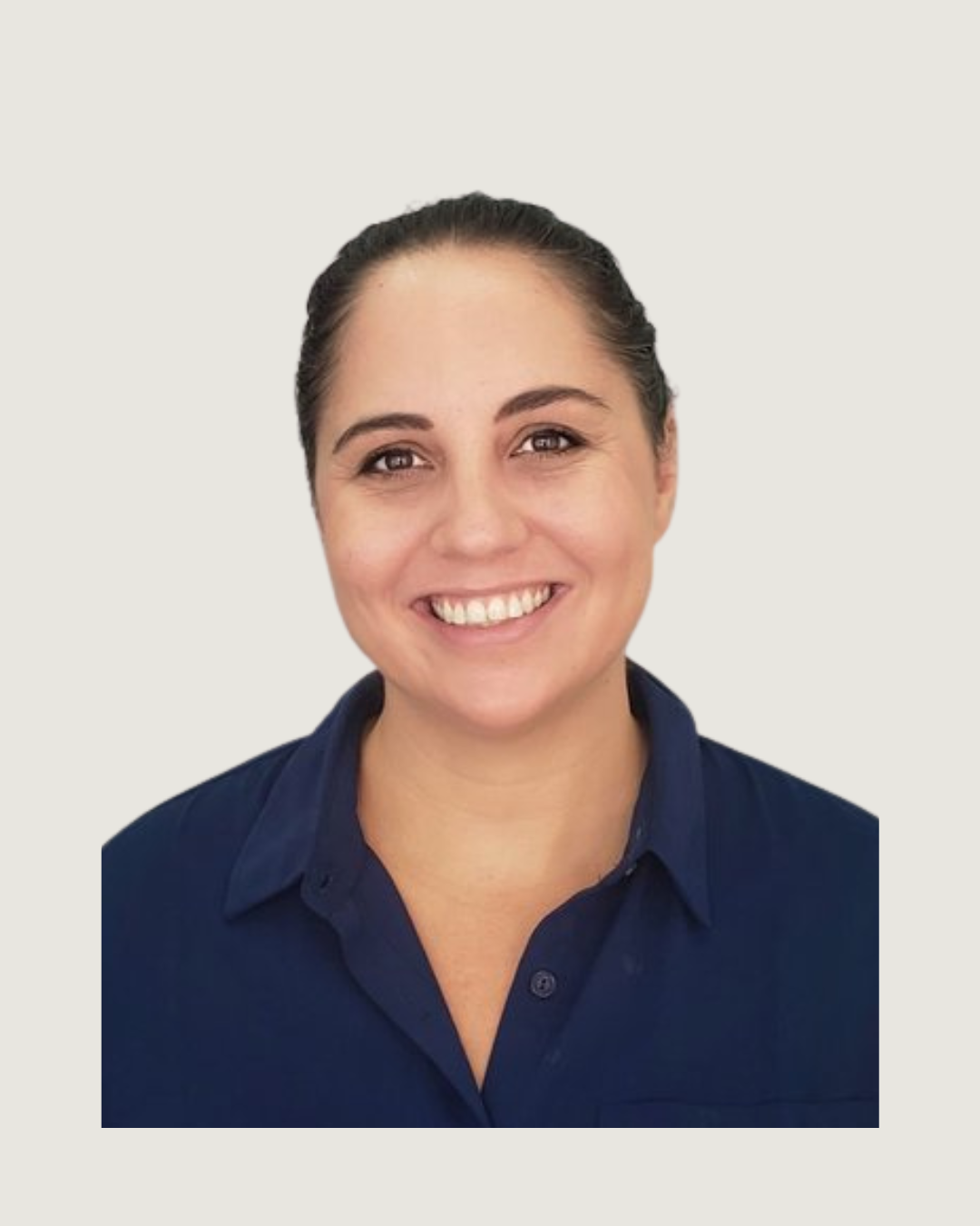 A woman with dark hair tied back, smiling, wearing a navy blue shirt, standing against a plain gray wall.