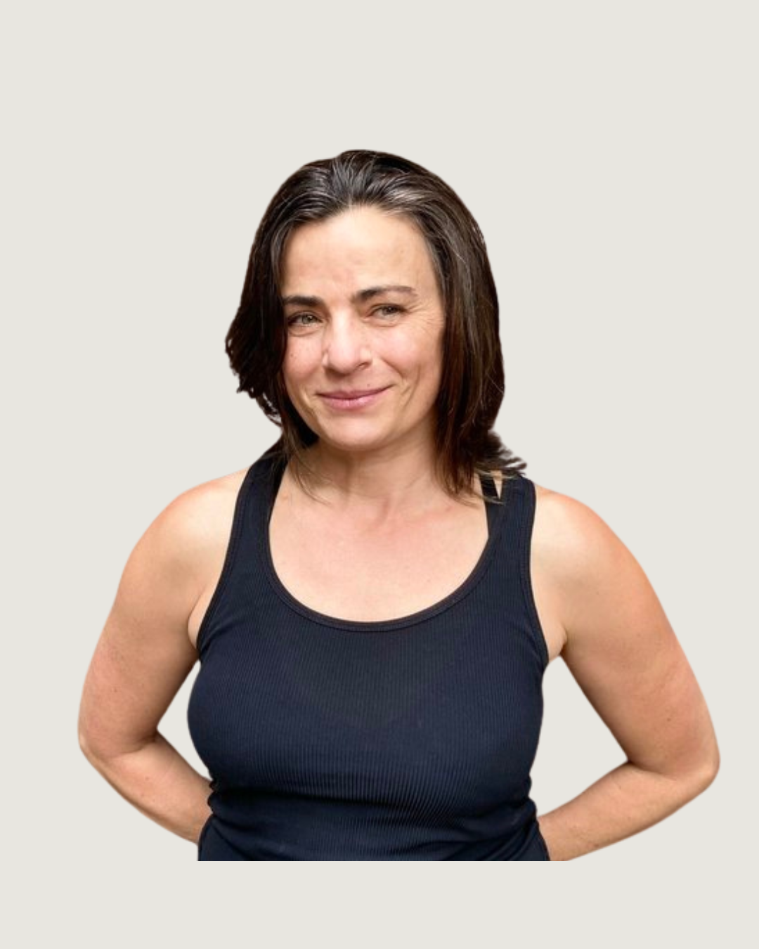 A woman with shoulder-length dark brown hair standing in front of a brick wall, wearing a black tank top, smiling slightly.