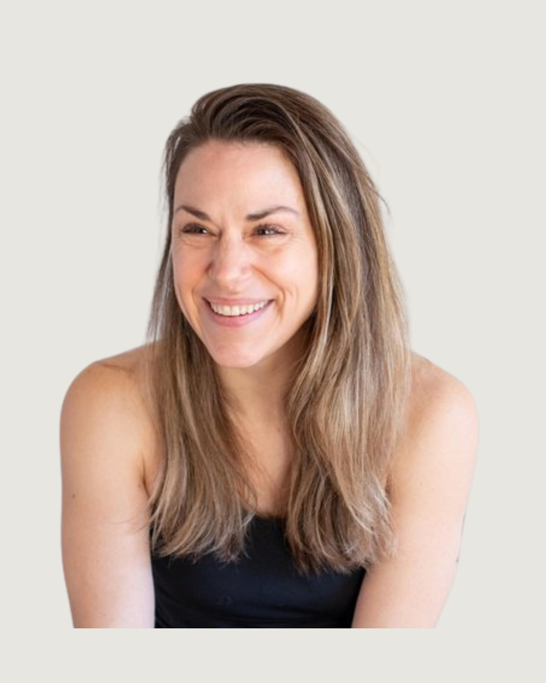 A woman with long brown hair and a black top smiling and looking to the side against a plain light-colored background.