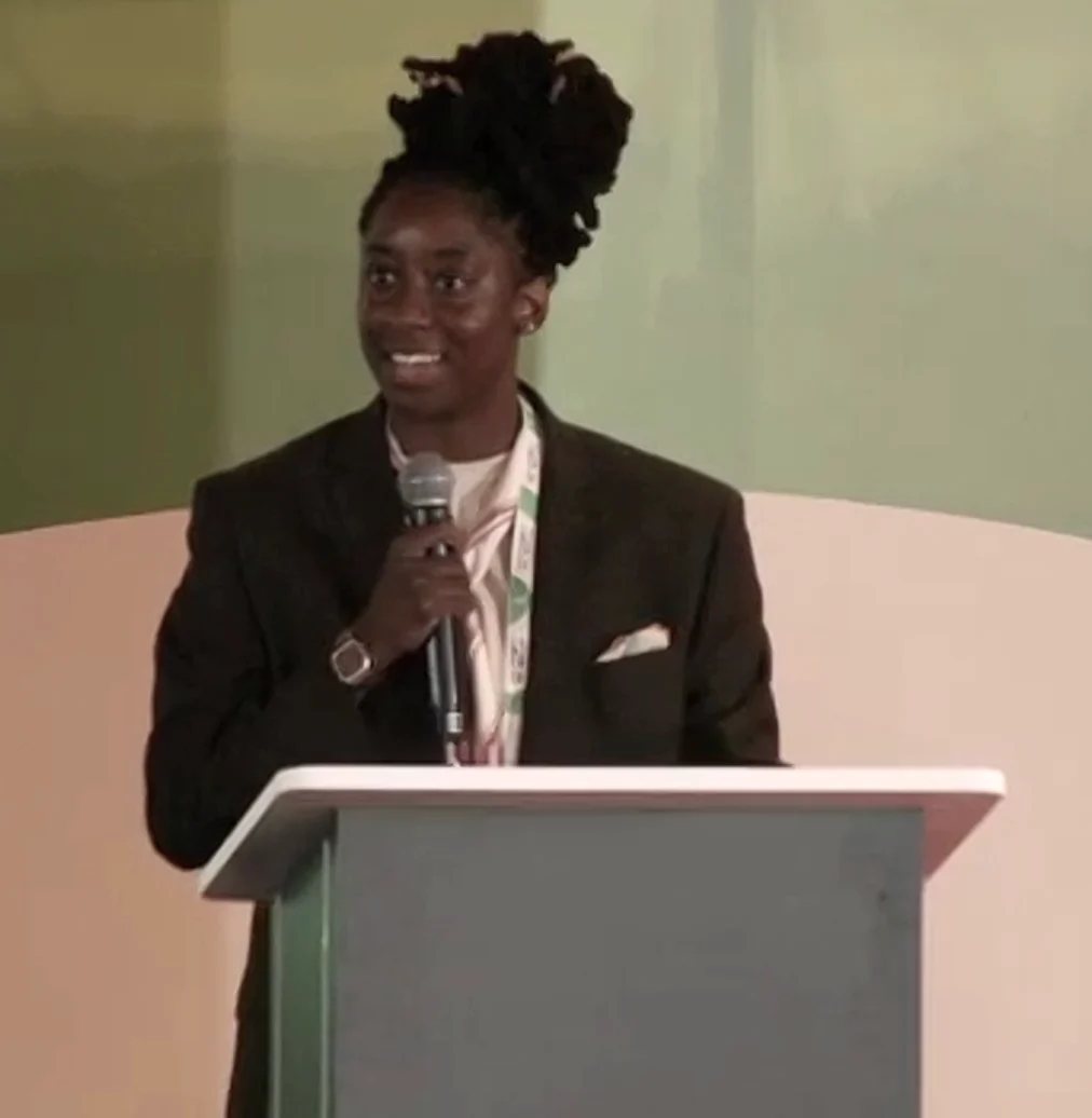 yemi knight standing at podium and holding a mic while delivering acceptance speech