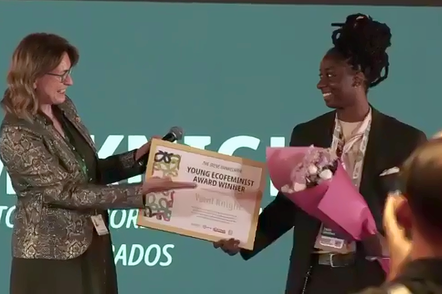 yemi knight smiling and holding a bouquet of flowers in one hand while accepting plaque that says 'young ecofeminist award winner'
