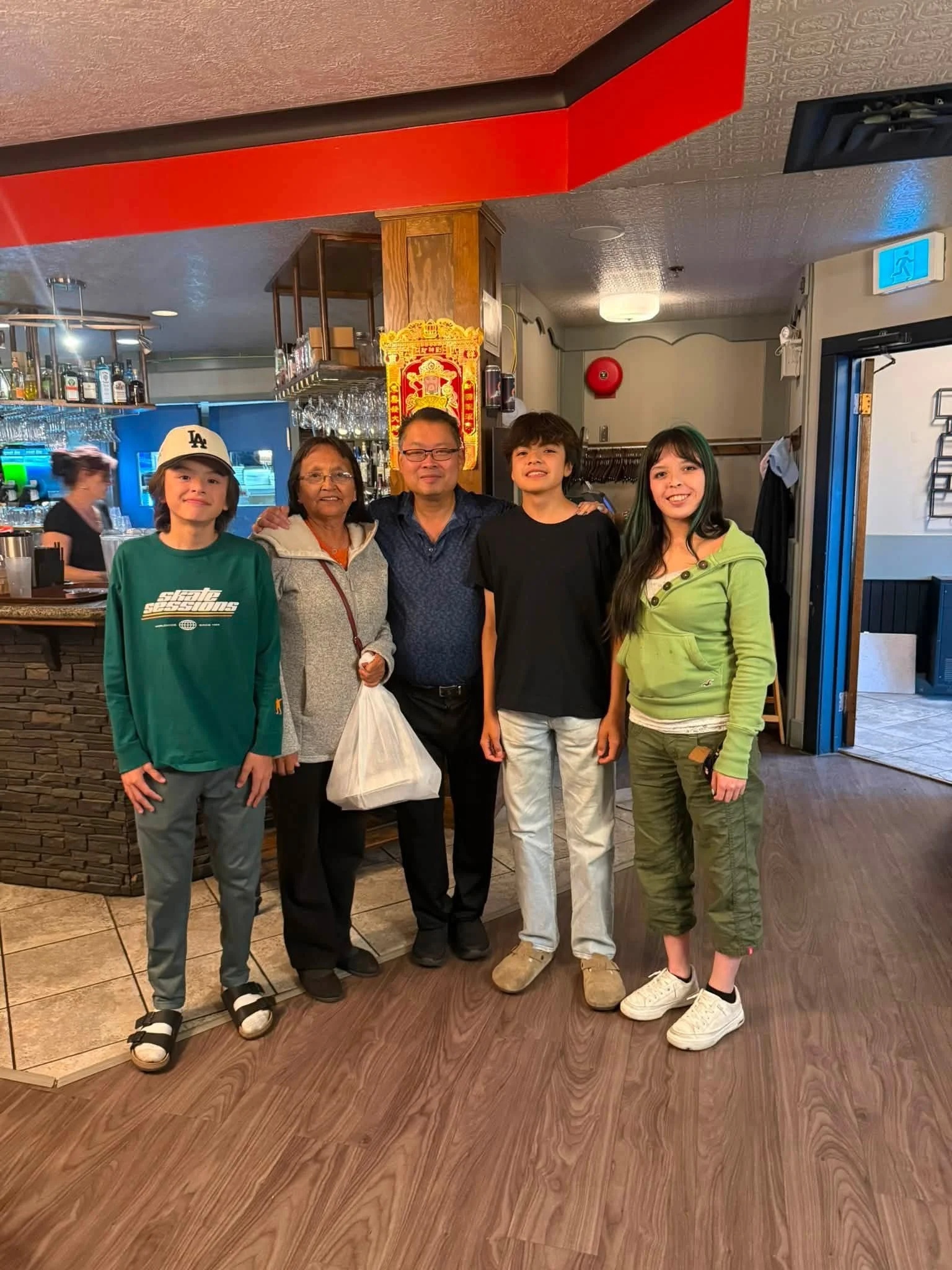 A group of five people, including children and adults, standing inside a restaurant near the bar area, smiling at the camera.