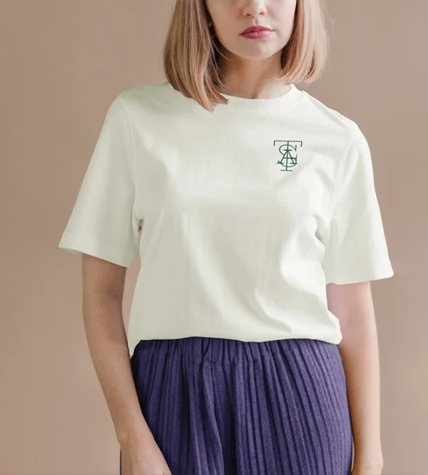 Woman wearing a white t-shirt with a custom-designed logo on the chest and purple pleated skirt against a neutral background.