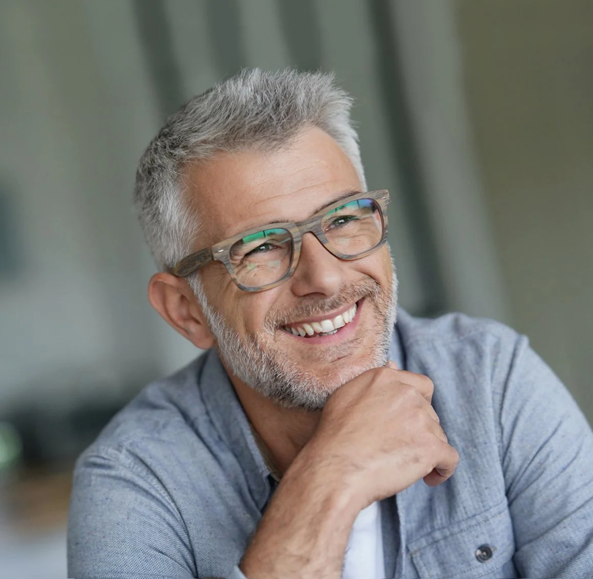 A middle-aged man with gray hair and glasses smiling and resting his chin on his hand.