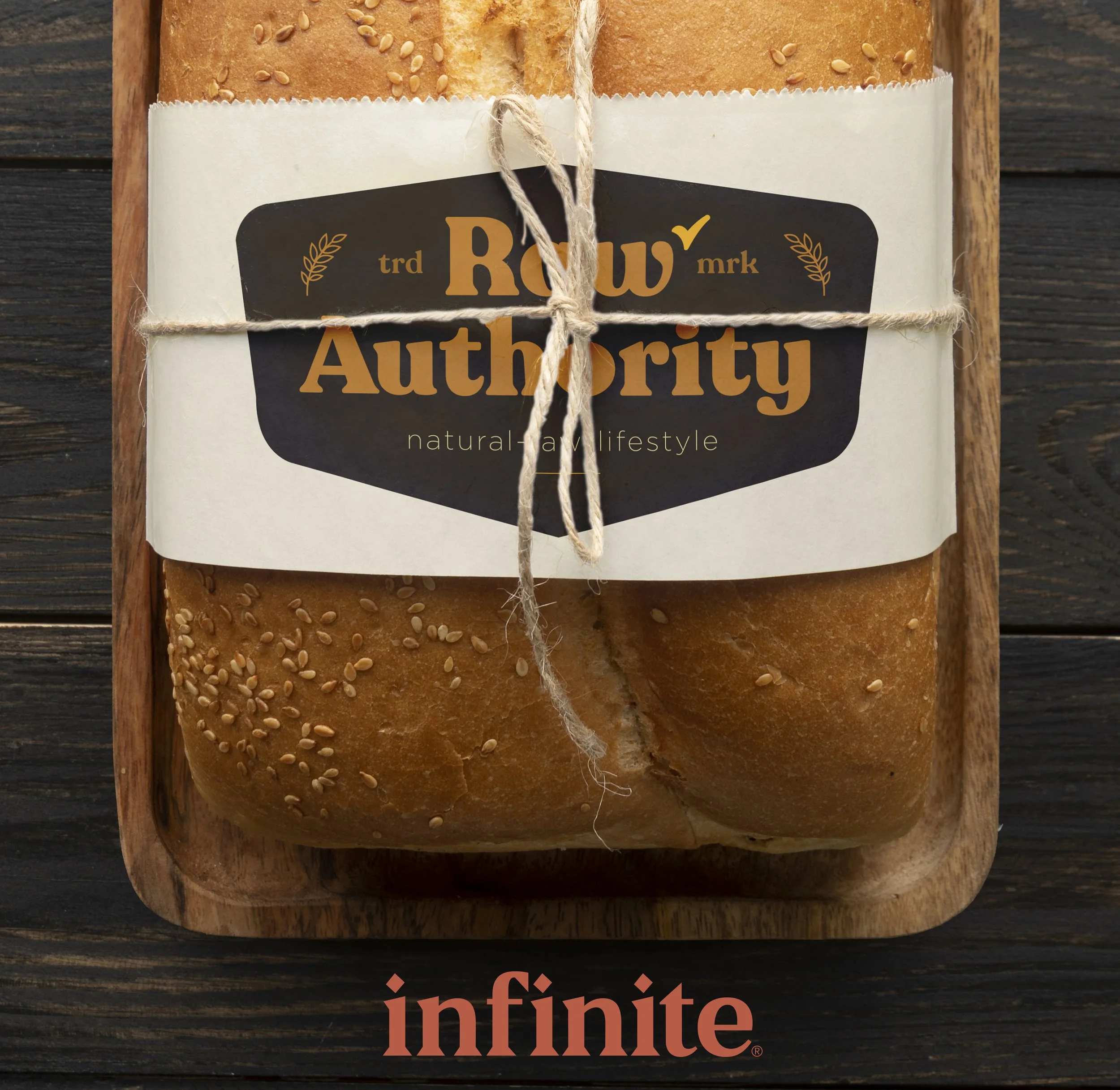 A loaf of bread with sesame seeds on top is wrapped with a label reading 'Raw Authority natural lifestyle' and tied with a string, placed on a wooden tray.
