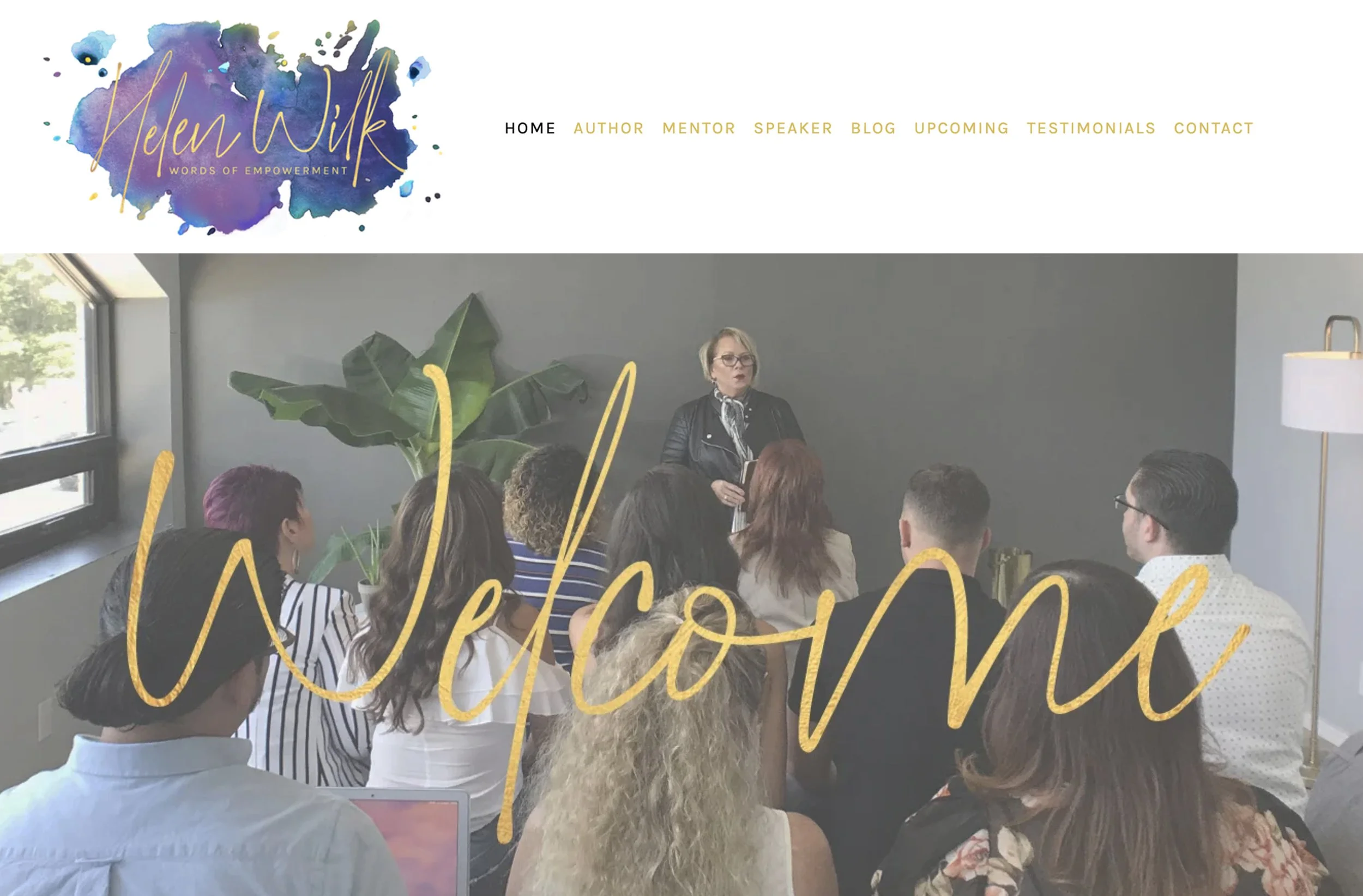 Photo of a Helen Wilk giving a presentation to a group of people in a room with large windows and a potted plant, with a large gold foil script that reads "Welcome."