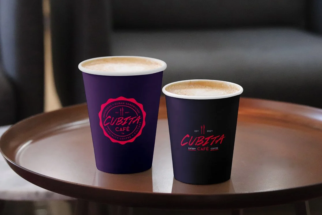 Two cups of coffee on a brown tray, with purple and black cups bearing the logo of Cubita Café, on a brown table designed by Infinite®.