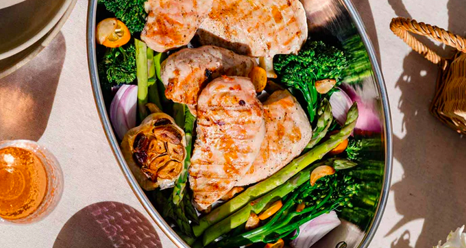 A platter of golden pasture raised chicken breasts surrounded by organic vegetables and a roasted garlic bulb.
