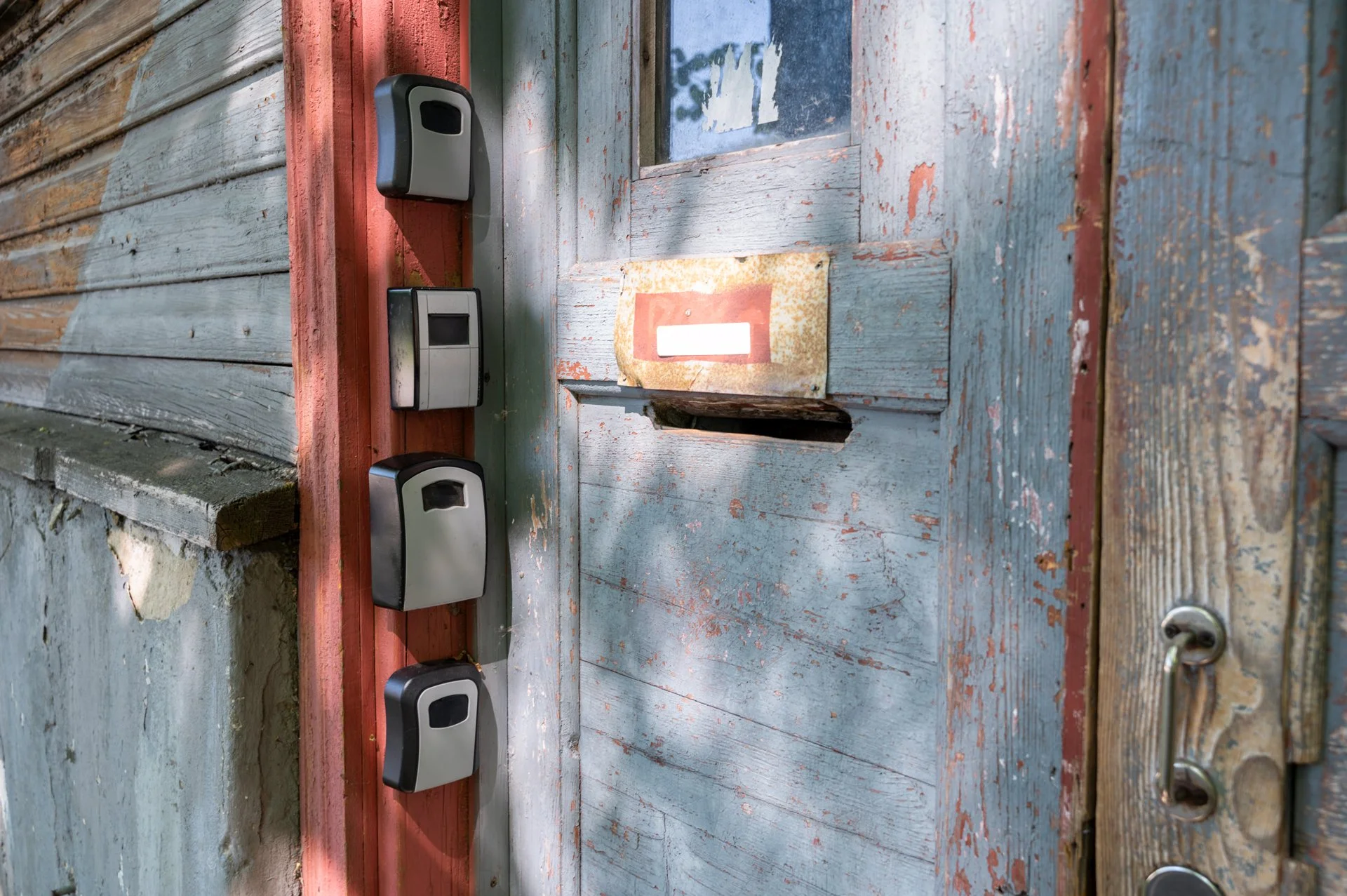 Four grey and black lockboxes for entry mounted on a wooden wall.