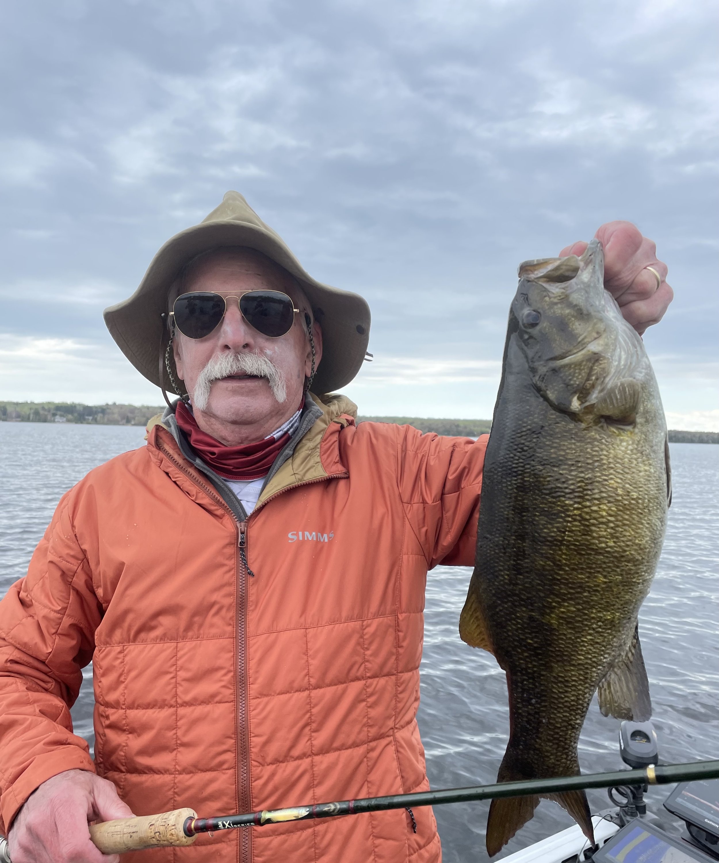 Bass Fishing Guide Services - Fishing Guide - Twin Lakes, MI - Man wearing sunglasses and orange jacket holding a large fish on a boat.