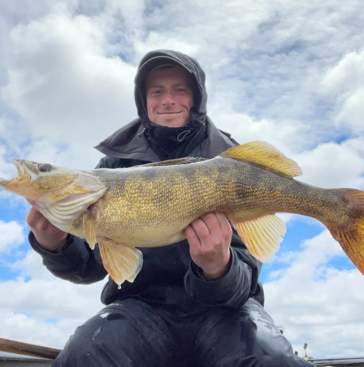 Bass Fishing Guide Services - Fishing Guide - Upper Michigan - Person holding a walleye fish with a cloudy sky background.