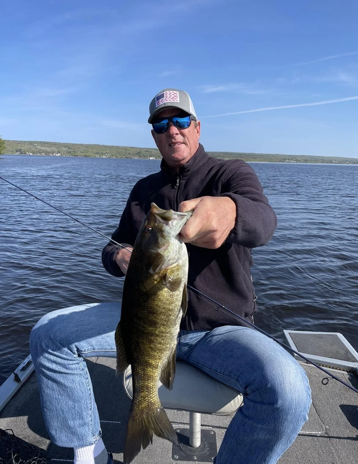 Person holding a fish on a boat with a lake in the background.