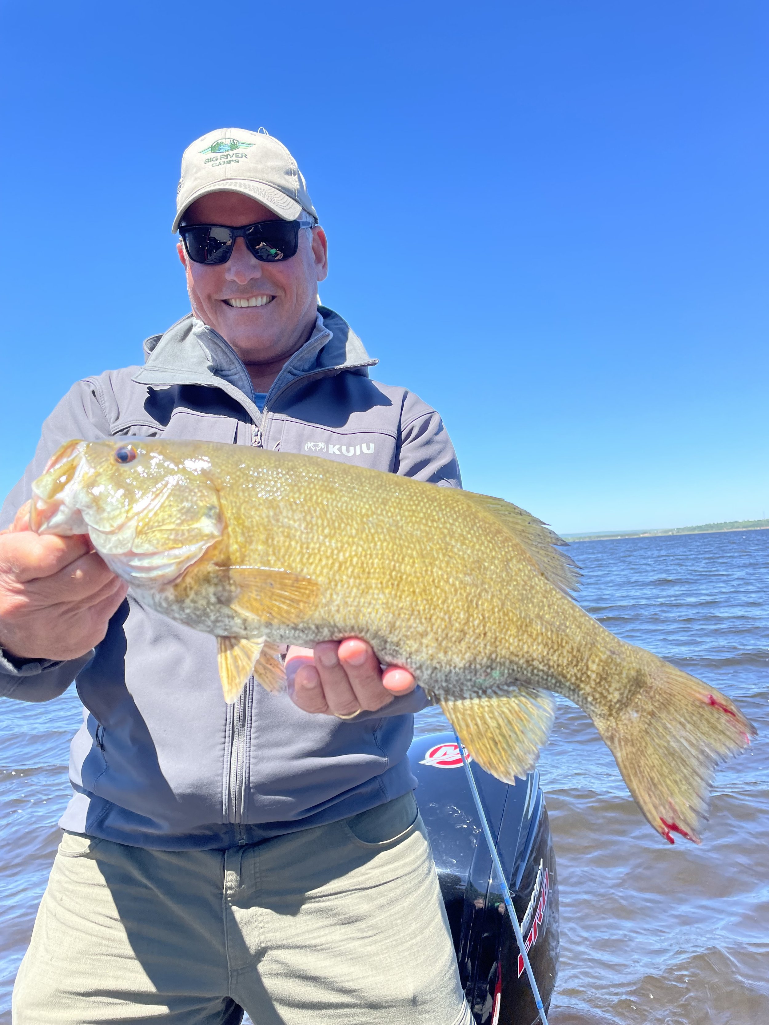 Man holding a large fish with a lake backdrop.
