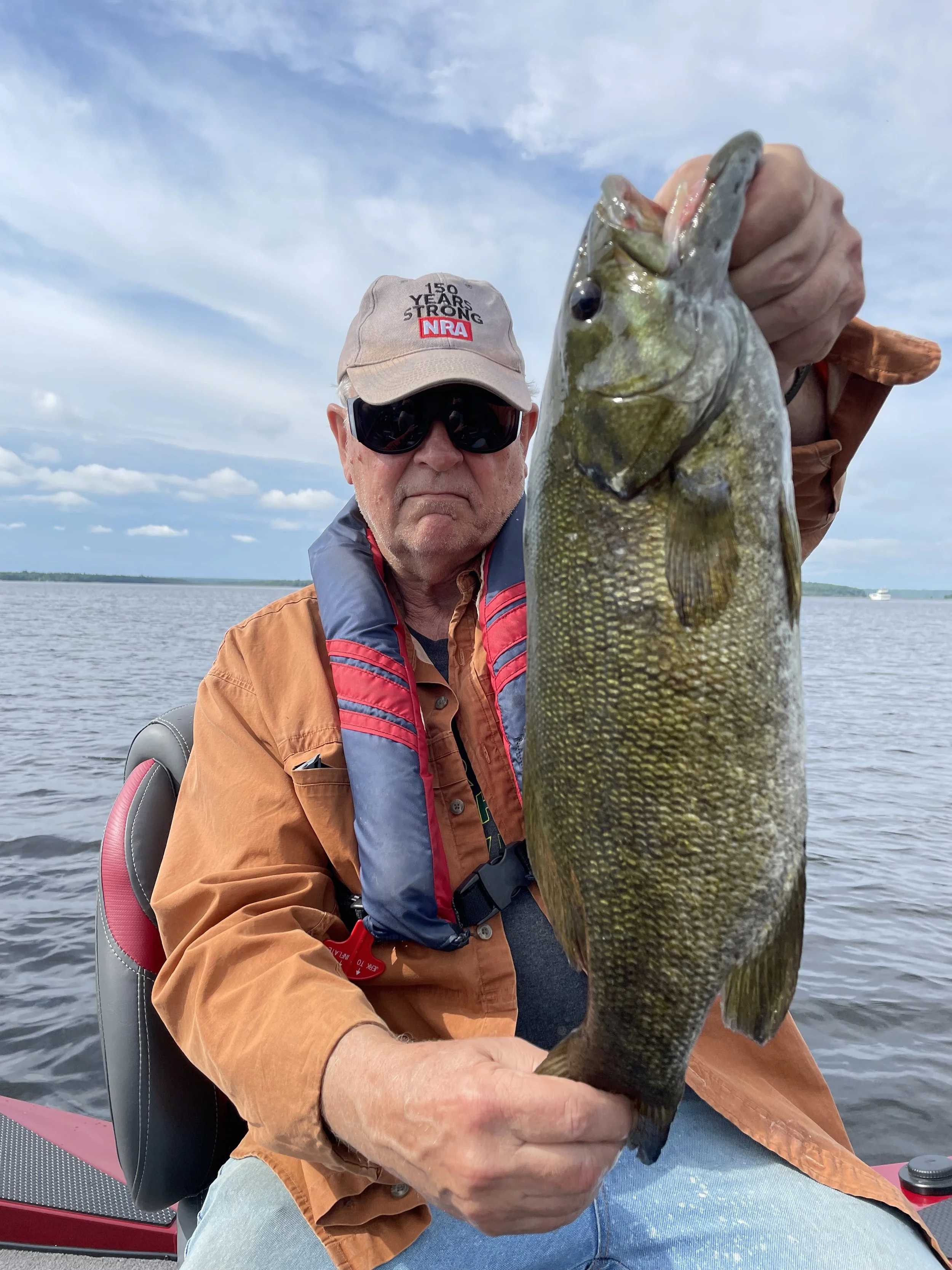 Bass Fishing Guide Services - Fishing Guide - Upper Michigan - Man wearing a cap and sunglasses holding a large fish on a boat.