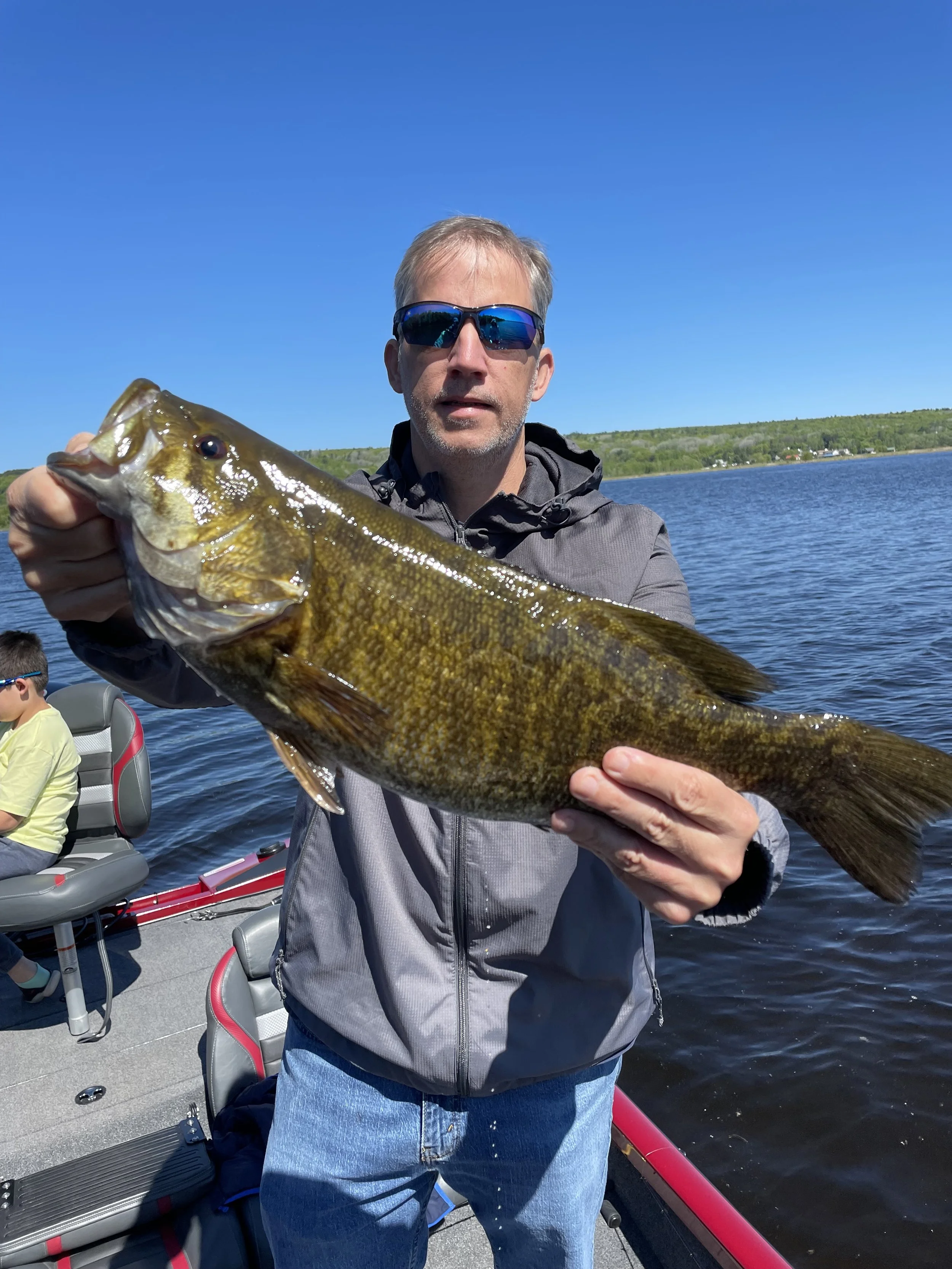 Person holding a large fish on a boat in a lake.