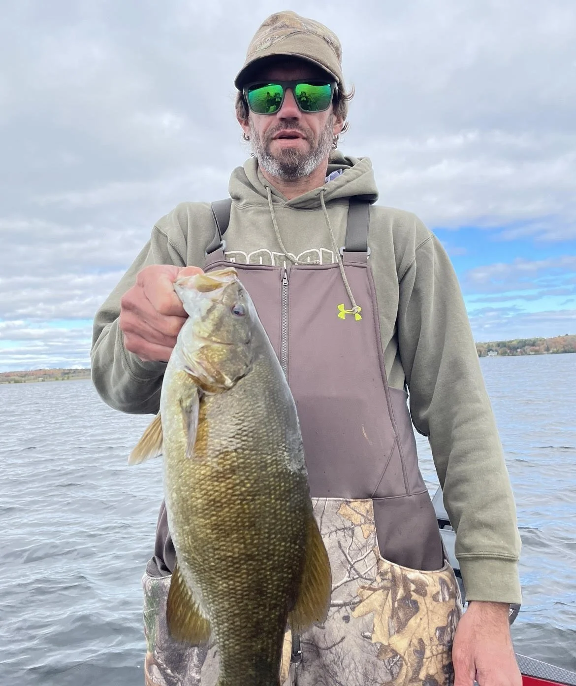 Person holding a large fish on a boat in a lake.