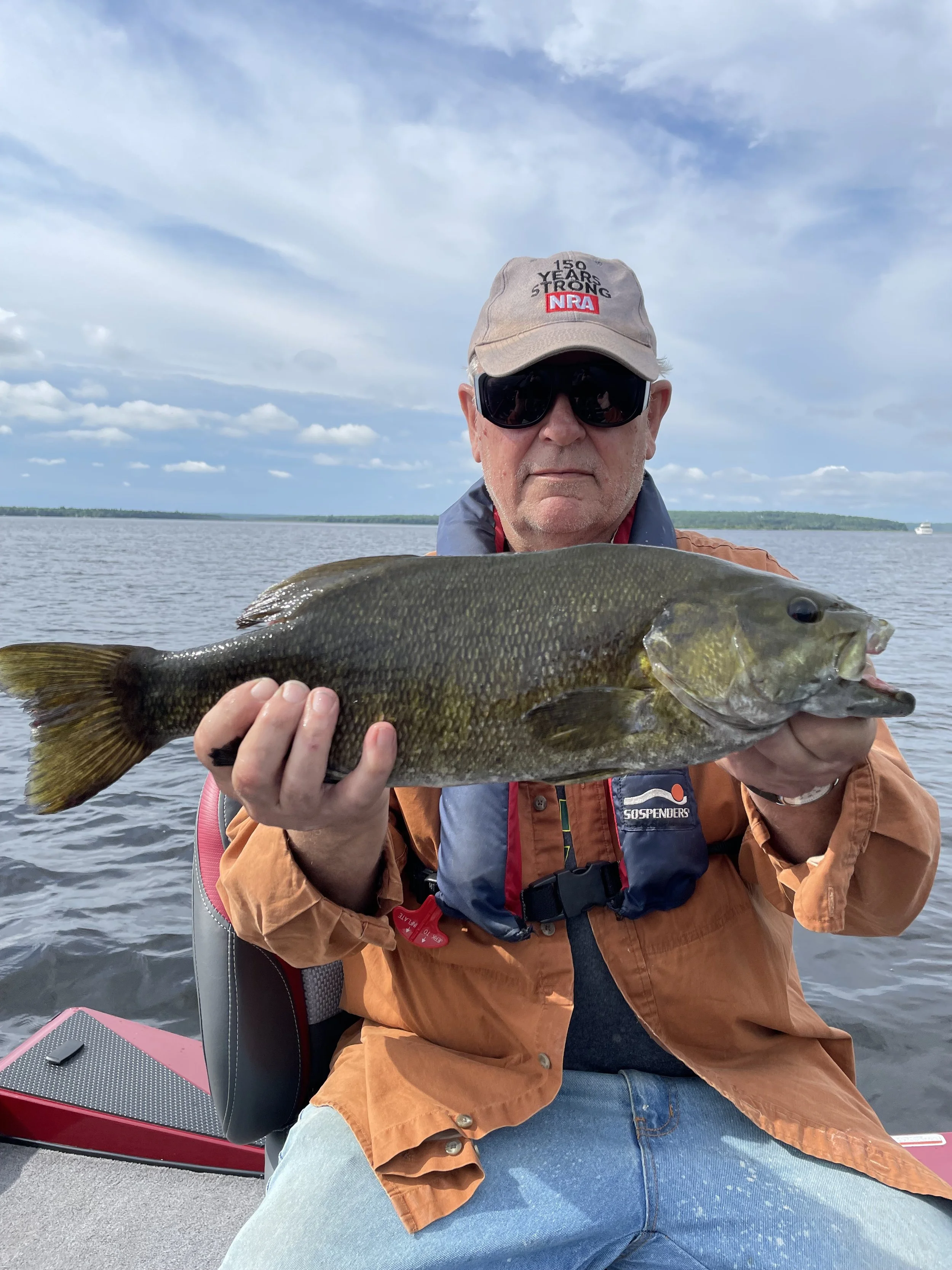 Bass Fishing Guide Services - Fishing Guide - Portage Lake, MI - Man holding a fish on a boat in a lake with cloudy sky.