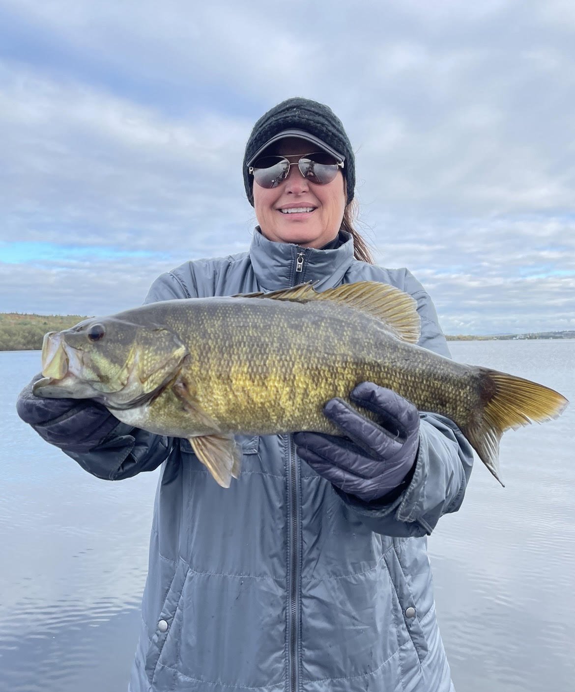 Person holding a large fish near a body of water on a cloudy day.