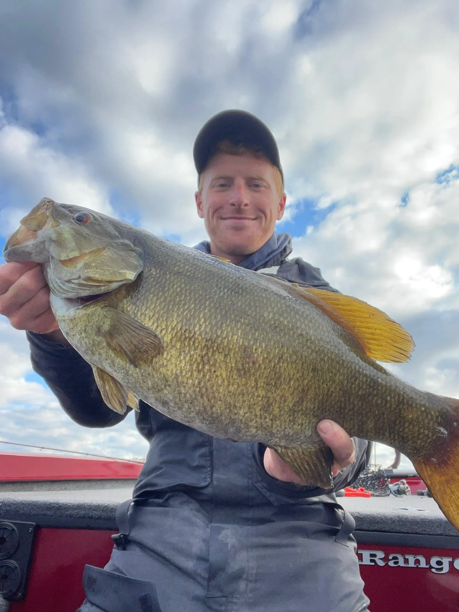 Bass Fishing Guide Services - Fishing Guide - Chassell, MI - Person holding a large fish on a boat under a cloudy sky.