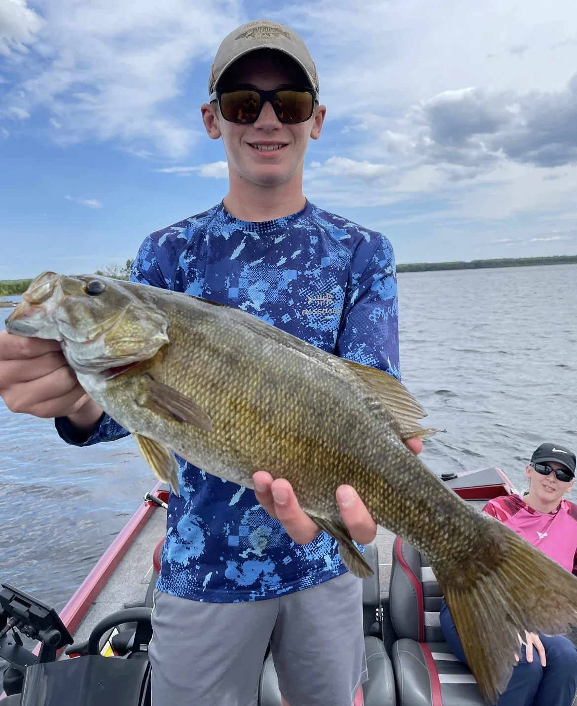A person holding a large fish on a boat, with water and sky in the background.