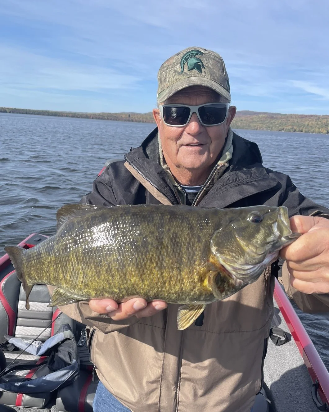 Bass Fishing Guide Services - Fishing Guide - Upper Michigan - Person holding a large fish on a boat with a lake in the background.