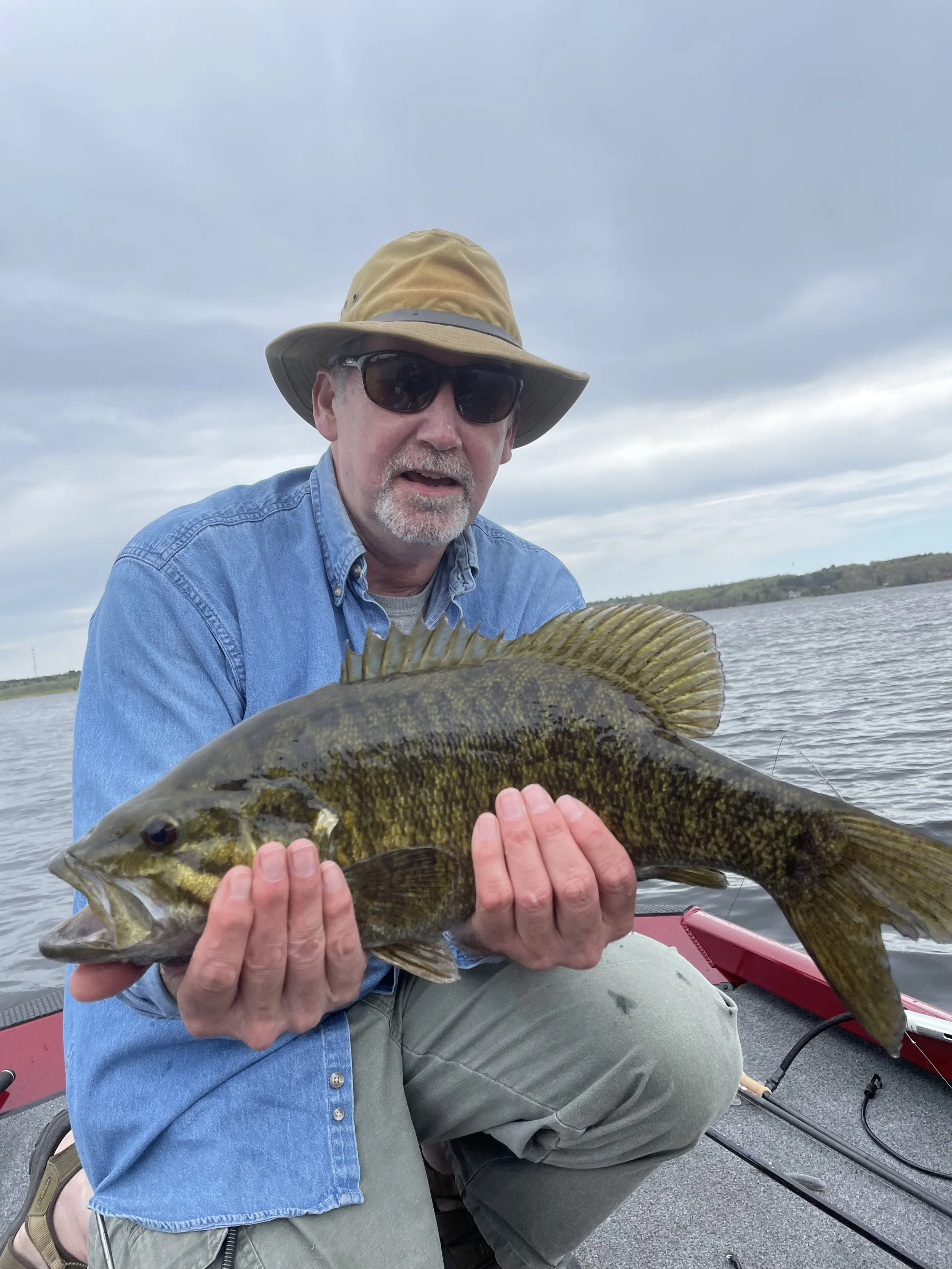 Bass Fishing Guide Services - Fishing Guide - Baraga, MI - Person wearing sunglasses and a hat holding a large fish on a boat.