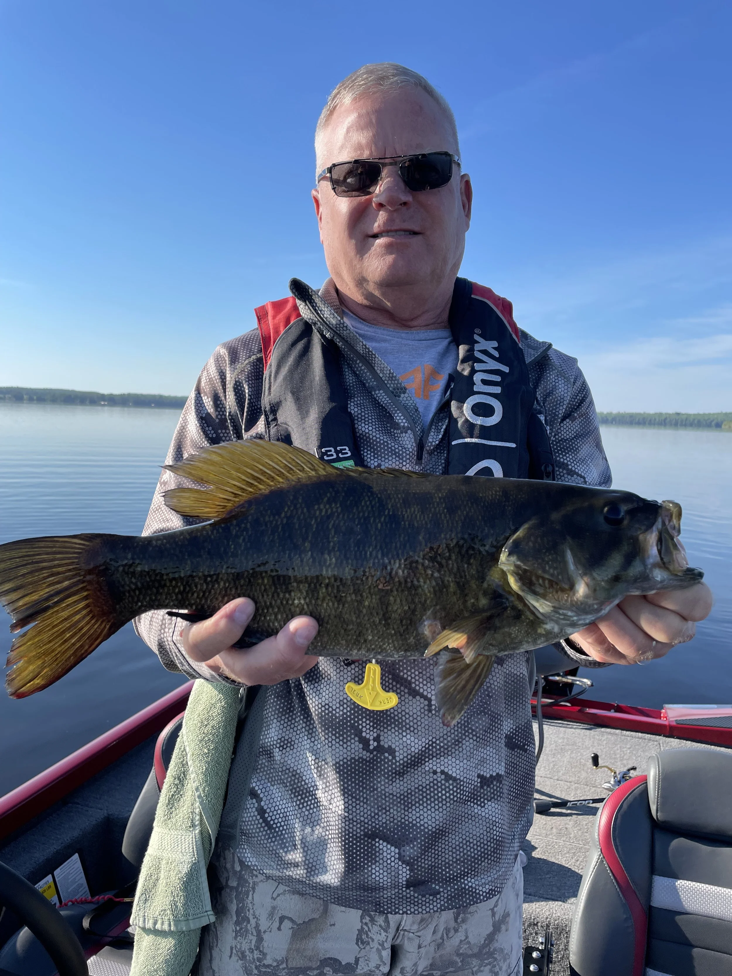 Bass Fishing Guide Services - Fishing Guide - Upper Michigan - Man holding a large fish on a boat with a lake in the background