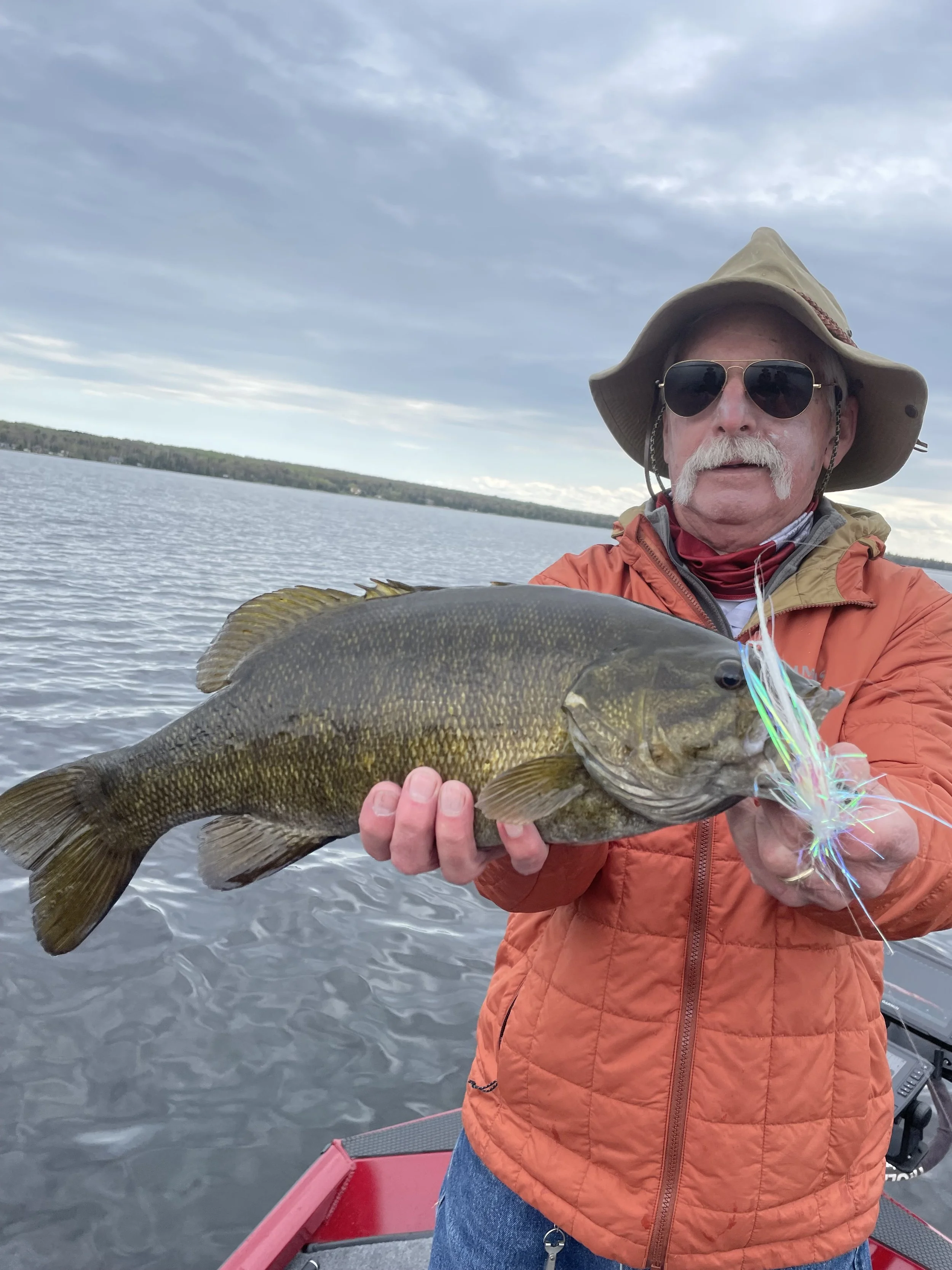 Man in hat holding a large fish on a boat in a lake.