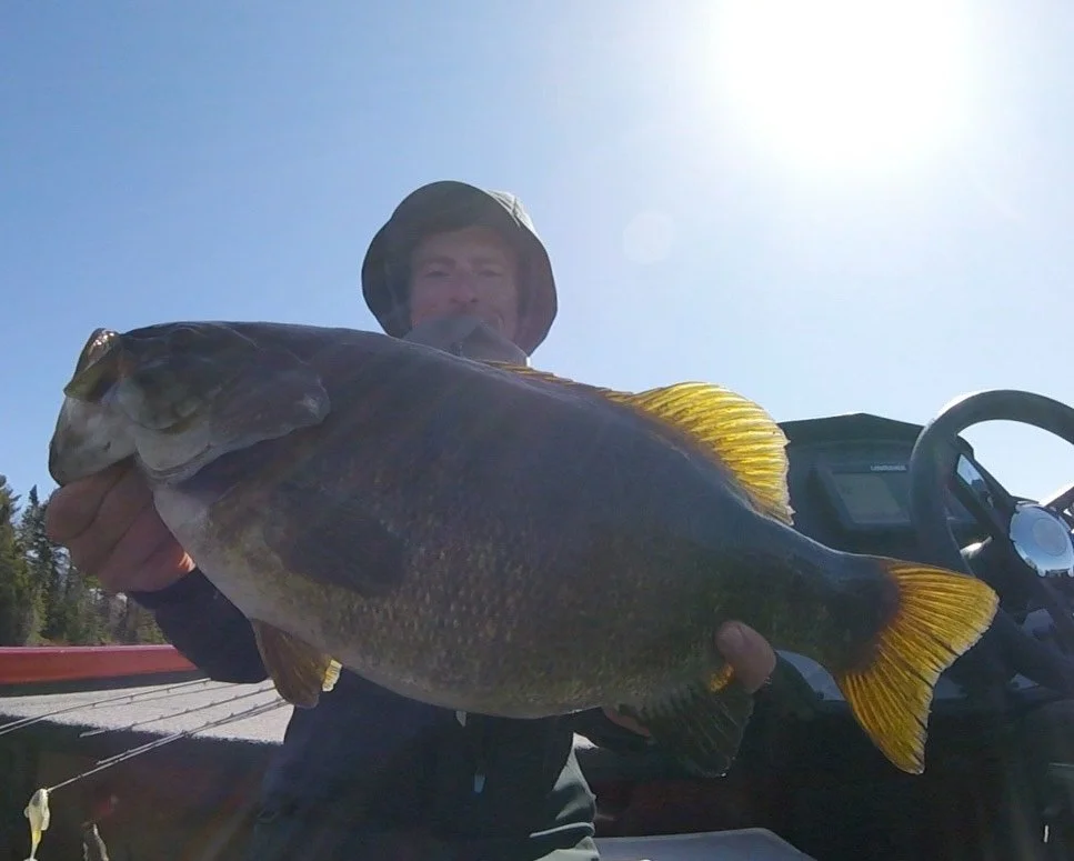 Bass Fishing Guide Services - Fishing Guide - Chassell, MI - Person holding a large fish on a boat under a bright sky.