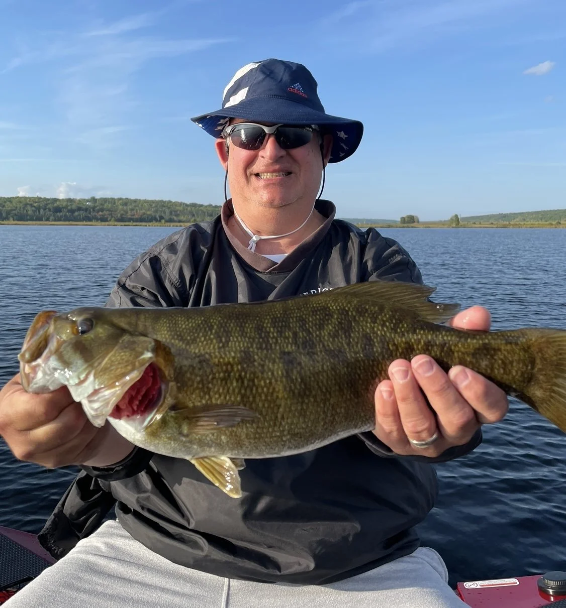 Bass Fishing Guide Services - Fishing Guide - Upper Michigan - Person holding a fish on a lake with a forest in the background.