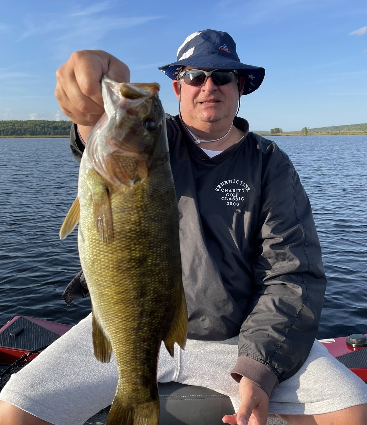 Bass Fishing Guide Services - Fishing Guide - Upper Michigan - Man holding a large fish while sitting on a boat, wearing sunglasses and a hat.