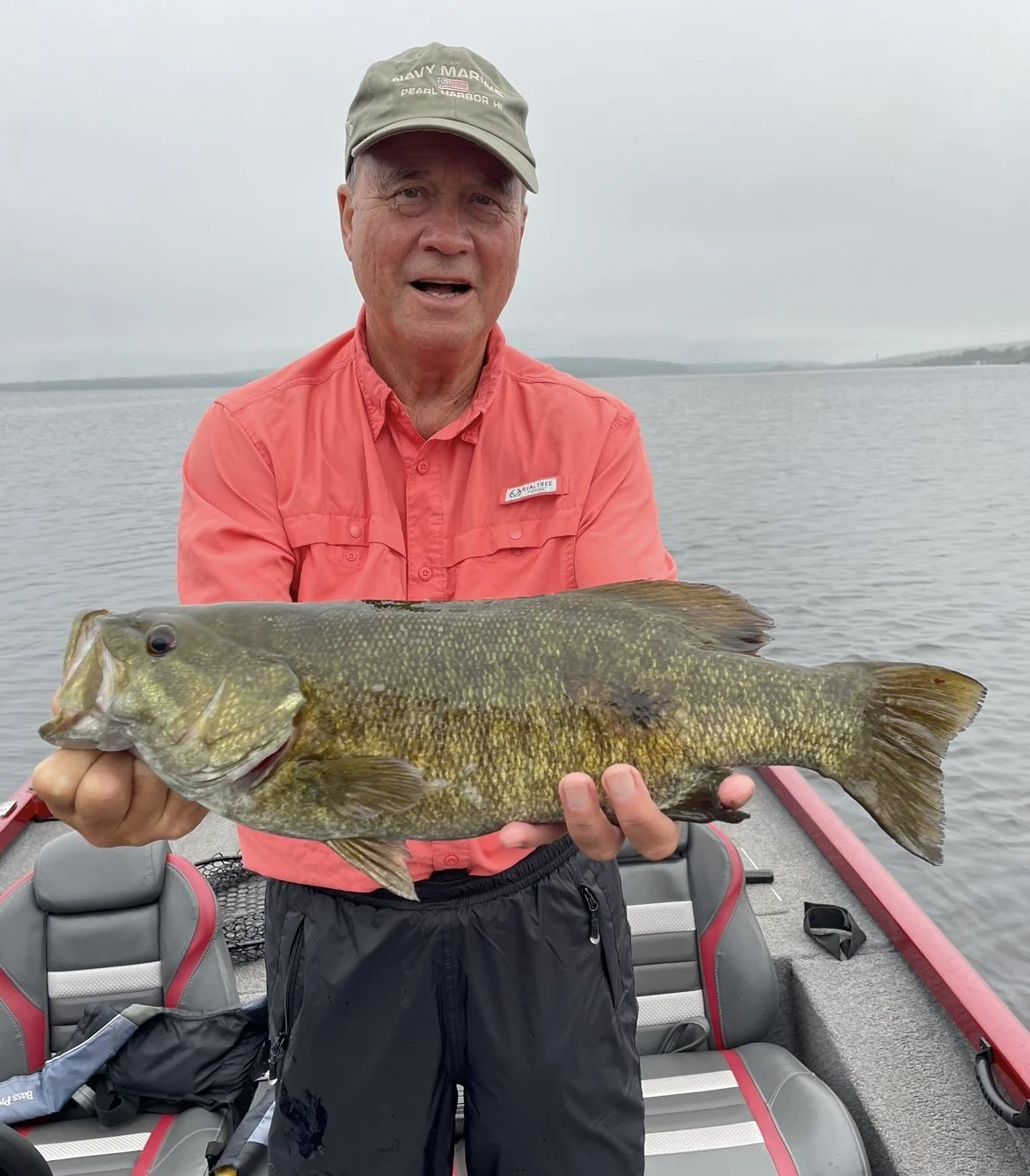 Person holding a large fish on a boat with water in the background.