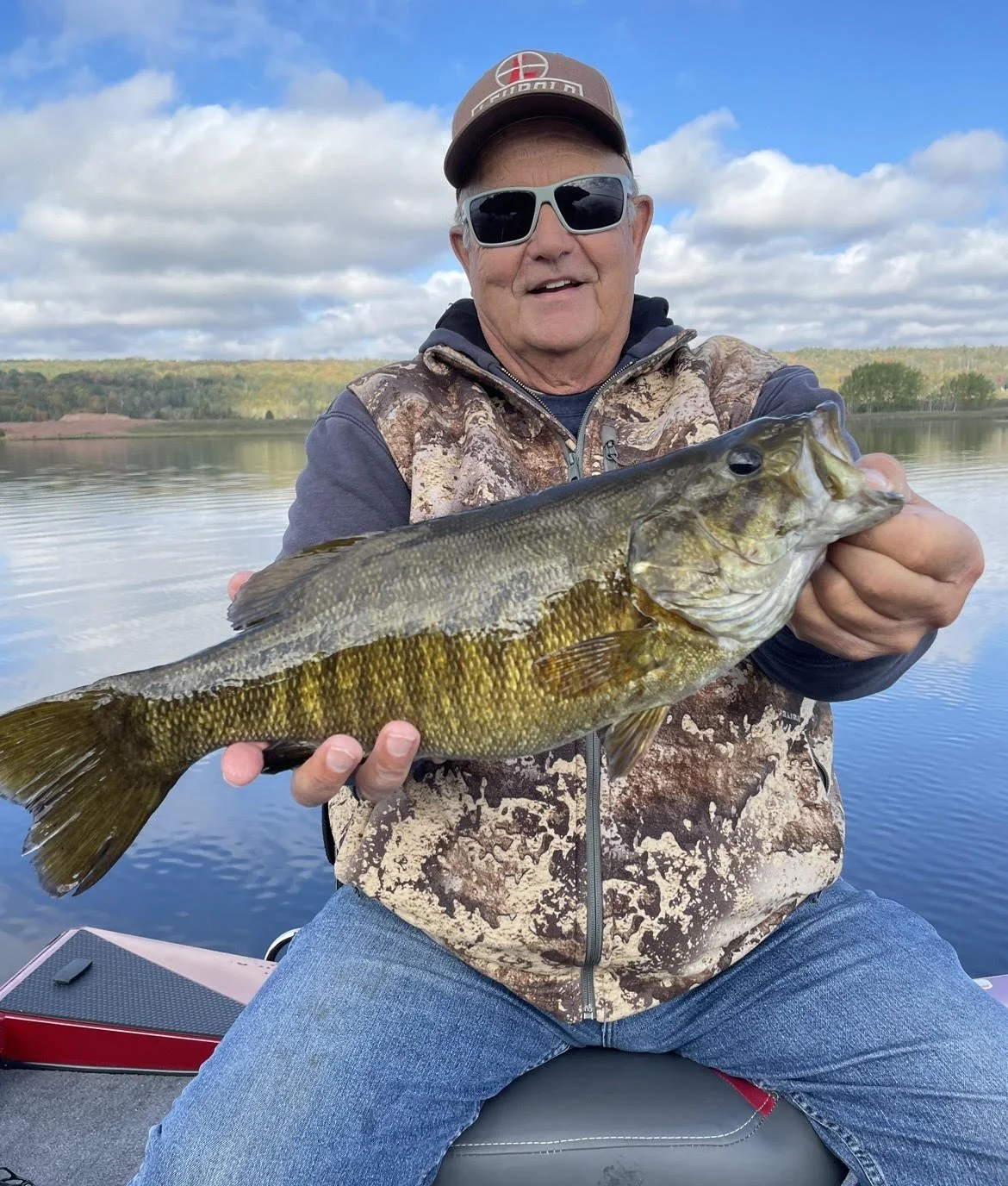 Man holding a largemouth bass while sitting in a boat on a lake.