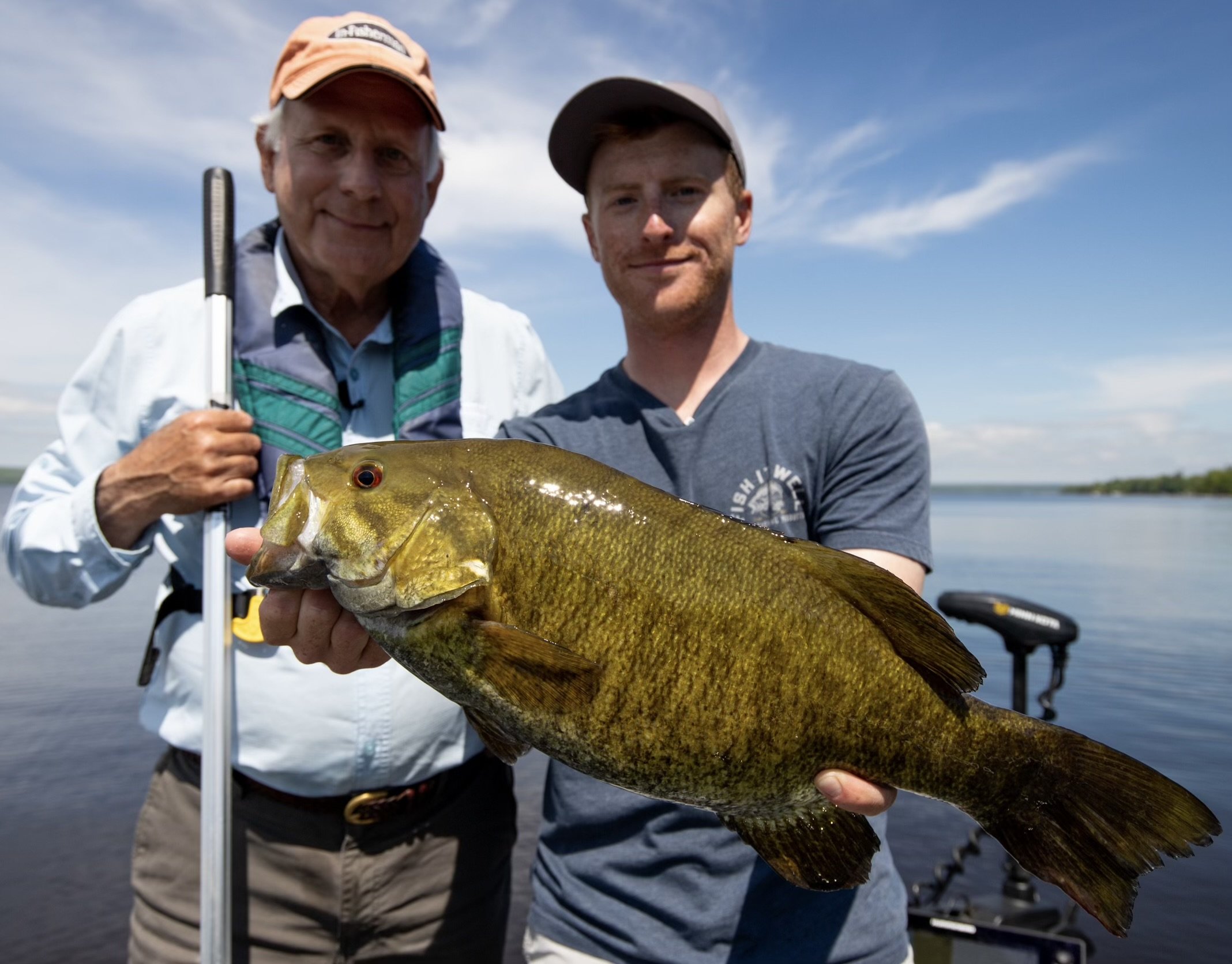 Bass Fishing Guide Services - Fishing Guide - Houghton, MI - Two men holding a large fish on a boat by a lake.