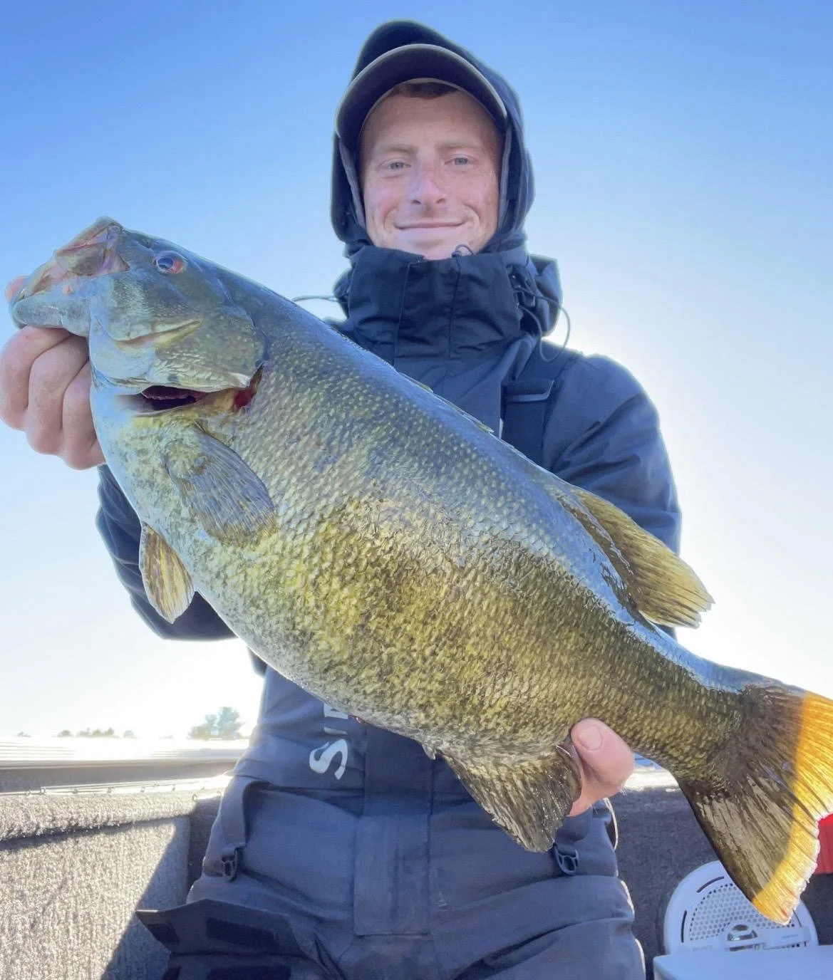 Bass Fishing Guide Services - Fishing Guide - Twin Lakes, MI - Person in outdoor gear holding a large fish on a boat.